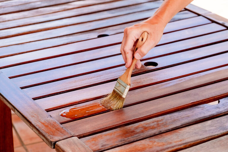 Applying deck stain to wooden table for outdoor living space enhancement