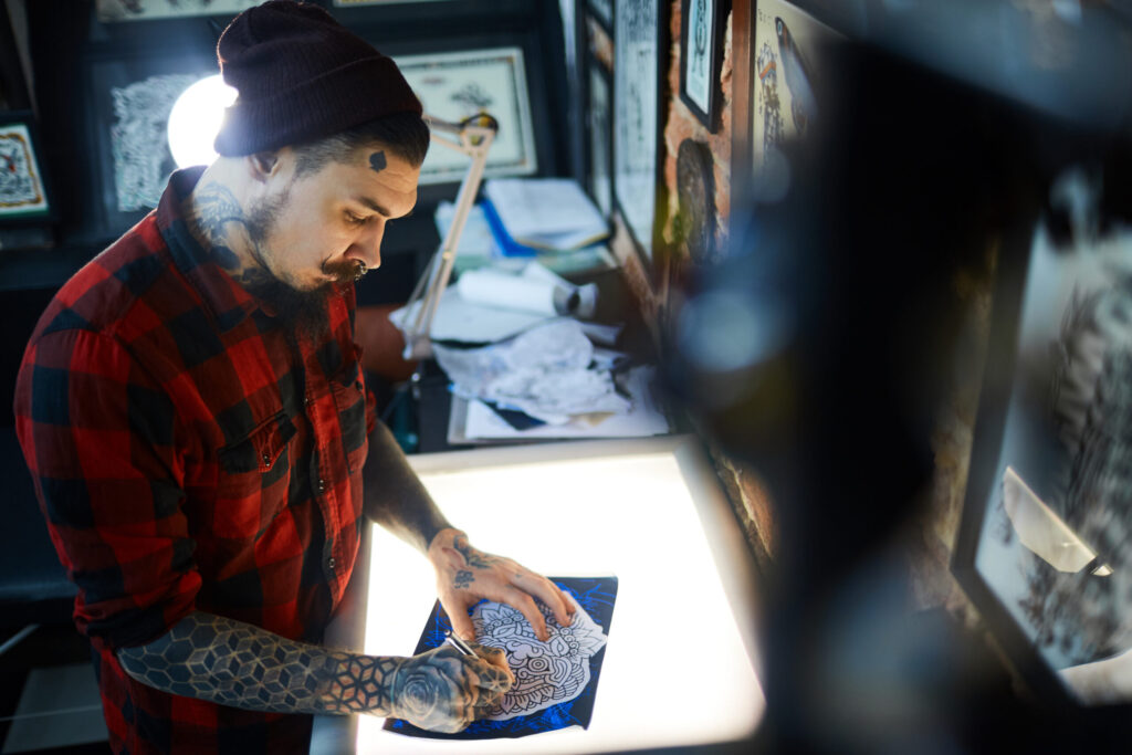 Tattoo artist sketching design on light box, preparing tattoo artwork.