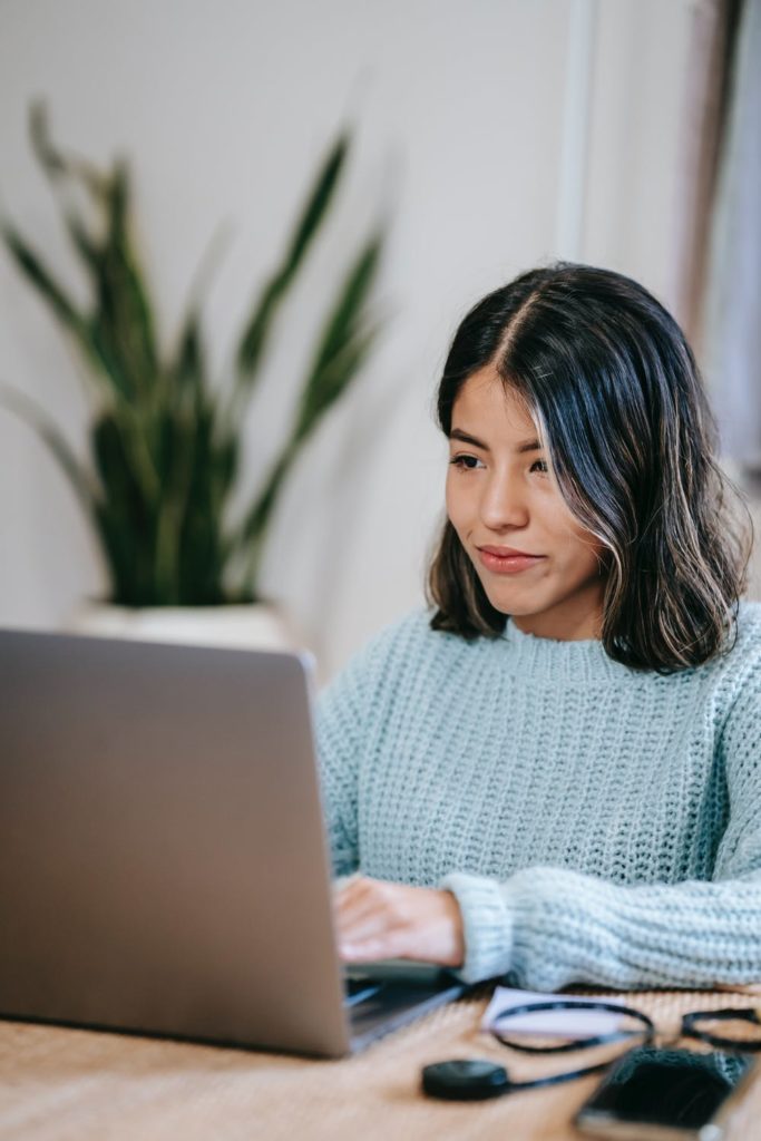 a woman sitting at a desk with a laptop and a plant