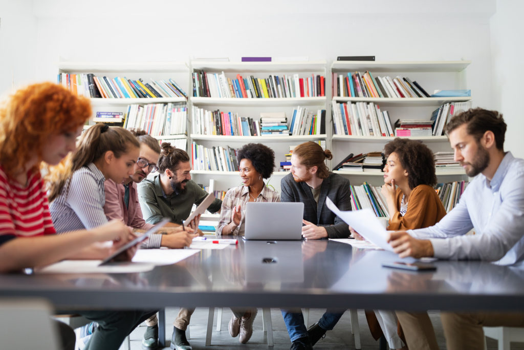 a group of people sitting around a table with laptops