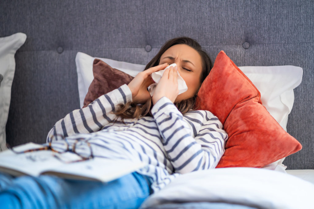 woman laying in bed sneezing