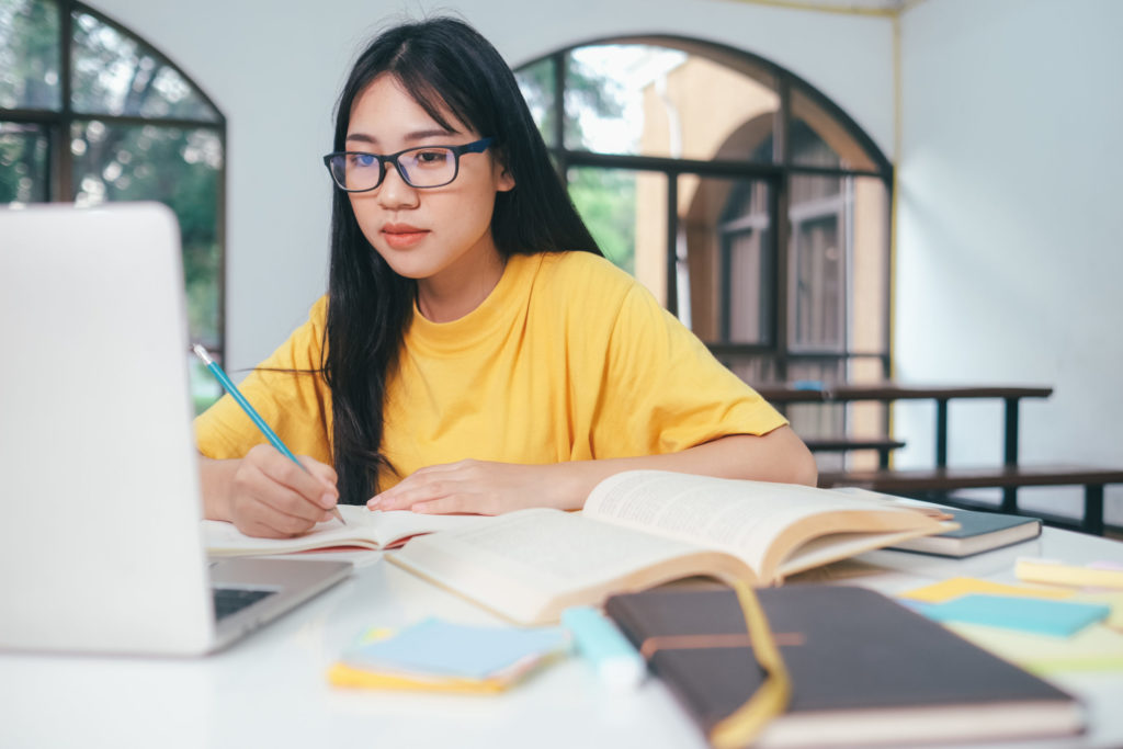 Young collage student using computer and mobile device studying online.